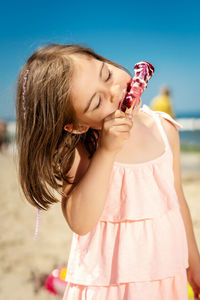 Cute girl with eyes closed eating ice cream at beach