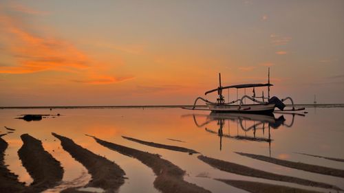 Silhouette boats moored on sea against orange sky