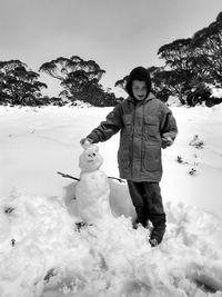 Boy standing by snowman against sky