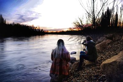 Rear view of women sitting by lake against sky