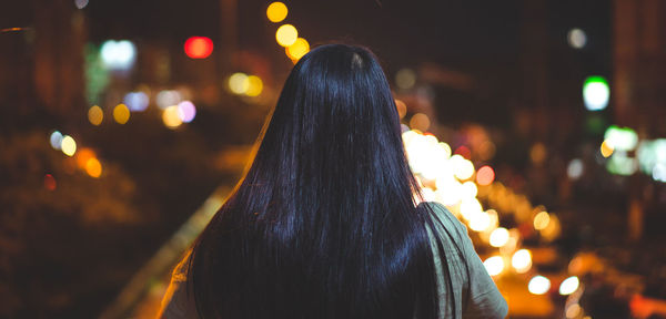 Rear view of woman looking at illuminated street in city