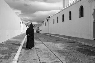 Rear view of woman walking on footpath amidst buildings against sky