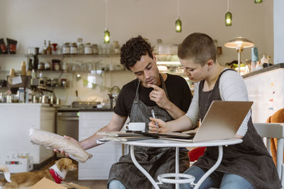 Male owner with hand on chin doing inventory with female colleague at cafe