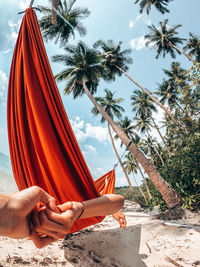 Close-up of man holding hand of woman lying in hammock at beach 