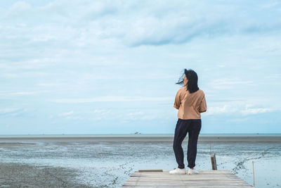 Woman standing on pier over sea against sky