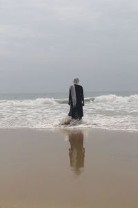 Rear view of men at beach against sky