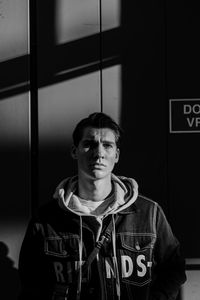 Portrait of young man standing against window