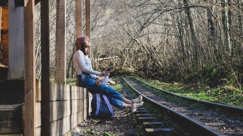 Side view of woman sitting on railroad track in forest