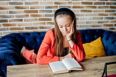 A young woman is sitting at home or in a cafe and reading a book.the girl is sitting on a soft sofa.