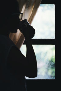 Side view of woman having coffee while standing by window