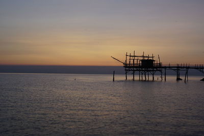 Silhouette pier over sea against sky during sunset