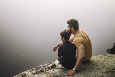 Father sitting with son on rock near lake