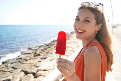 Beautiful young woman smiling with an icicle popsicle in her hand on summer. looks at camera.