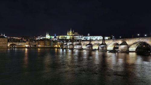 Illuminated bridge over river against sky at night