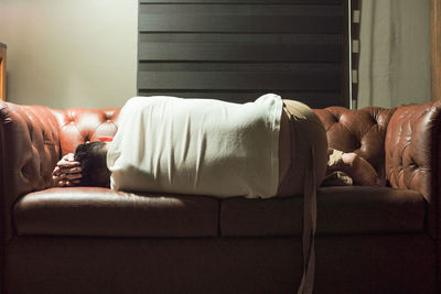 Rear view of man sleeping on sofa at home