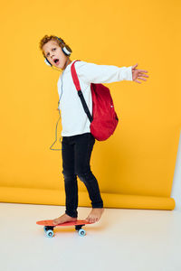 Full length of woman with arms raised standing against yellow background