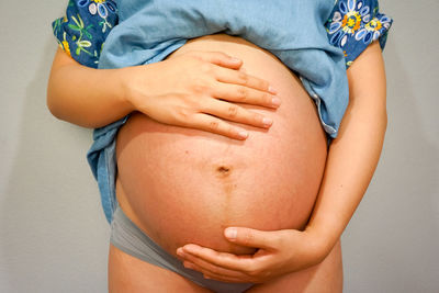 Midsection of pregnant woman in nightwear standing against wall