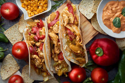 Still life of three fajitas or mexican tacos with meat, pepper, tomato, spicy pepper and nachos.