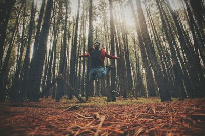 Low angle view of man jumping in forest by trees