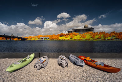 Canoes at lakeshore against sky in city during autumn