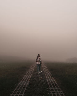 Rear view of man standing on railroad track against sky