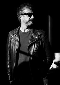 Young man wearing sunglasses standing against black background