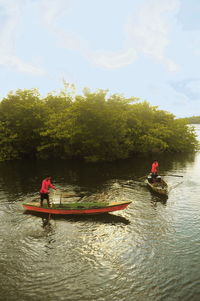 People rowing boat in river against sky