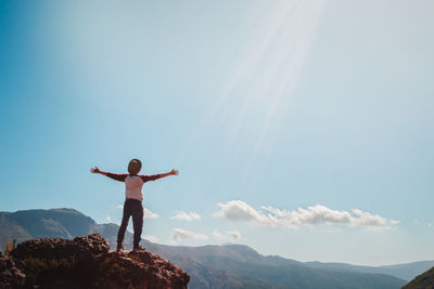 Rear view of man with arms outstretched standing on cliff against sky