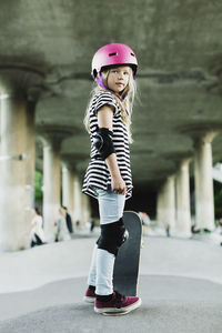 Full length of confident girl standing with skateboard at park