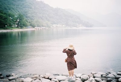 Rear view of woman standing on rocks by lake