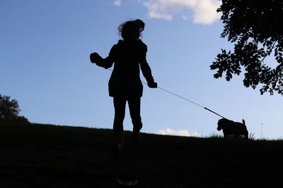 Silhouette man with dog on field against sky