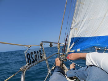 Low section of man on sailboat sailing in sea against clear blue sky