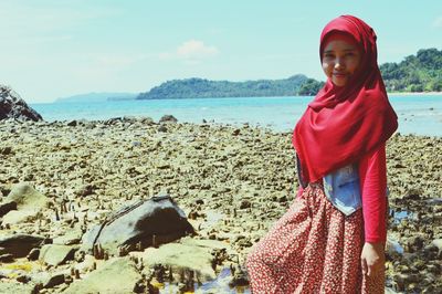 Portrait of young woman standing at beach against sky