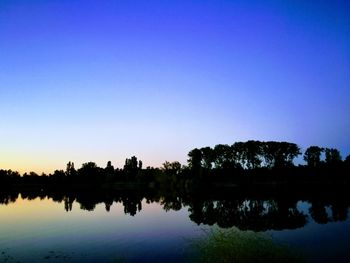 Reflection of silhouette trees in lake against clear sky