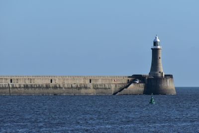 Lighthouse by sea against clear blue sky