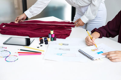 Midsection of fashion designers working while taking measurement of textile on table in office