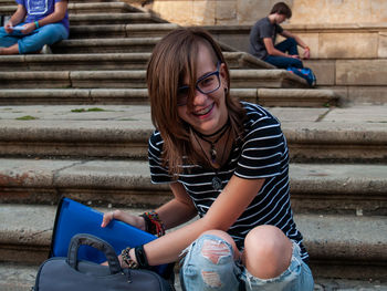 Full length of young woman holding file while sitting on steps against building