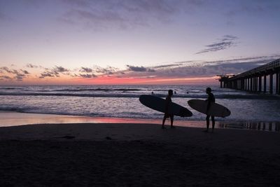 Silhouette male surfers standing at beach during sunset