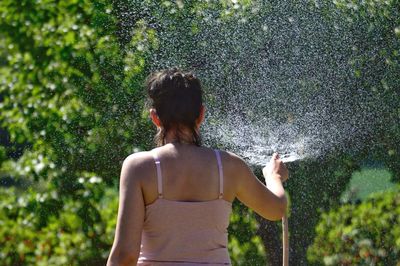 Rear view of woman spraying water in garden during sunny day