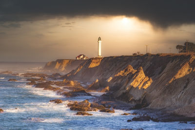 Lighthouse by sea against sky during sunset