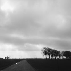 Road passing through field against cloudy sky