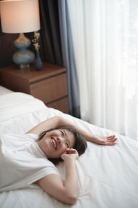 High angle view of smiling woman lying on bed at home