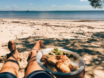 Low section of man holding food plate while relaxing at beach