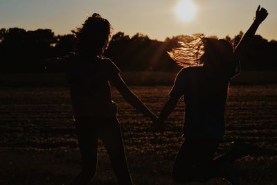 Rear view of silhouette children standing on field against sky during sunset