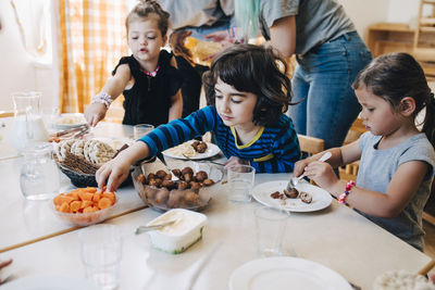 Students eating lunch at table against teachers standing in classroom