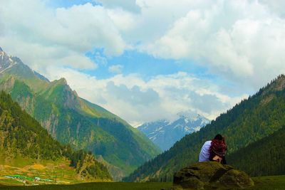 Rear view of woman sitting on mountain against sky