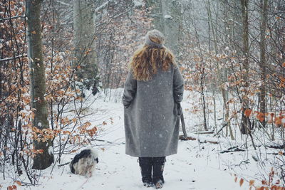 Rear view of dog and woman walking in snow covered forest