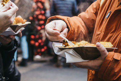 Unidentifiable people holding container with take away seafood paella, eating with plastic forks.