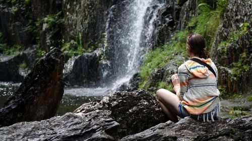 Rear view of woman sitting on rock in forest