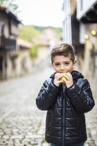 Portrait of smiling boy eating apple while standing on street